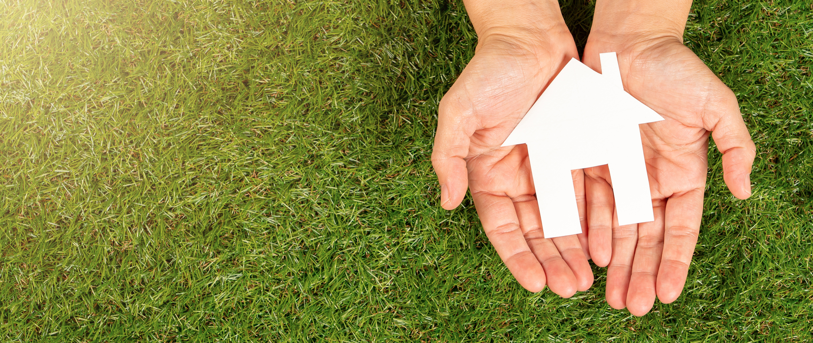 Hands holding a house cutout on a bed of grass